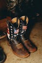 Stylish cowboy boots with American flag design on rustic floor.