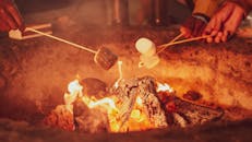 Close-up of hands roasting marshmallows over a campfire at night, creating a cozy atmosphere.